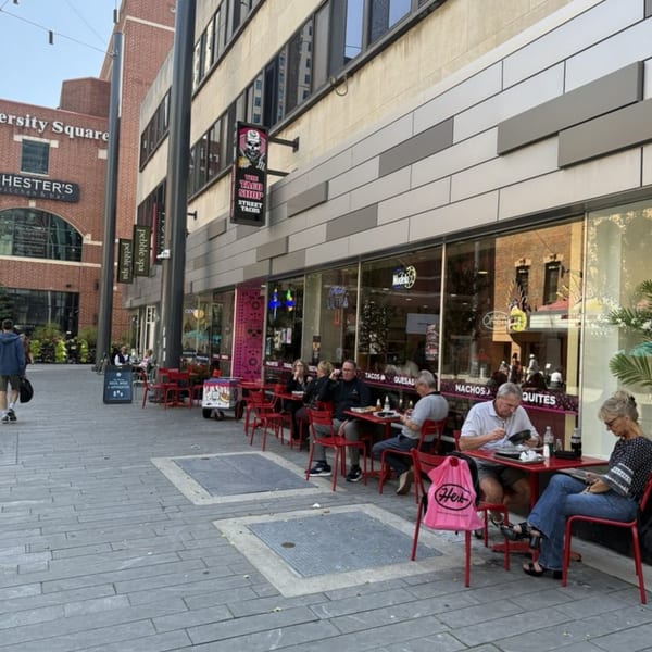 The Taco Shop's outdoor patio with red tables and chairs, and people dining on a city sidewalk.