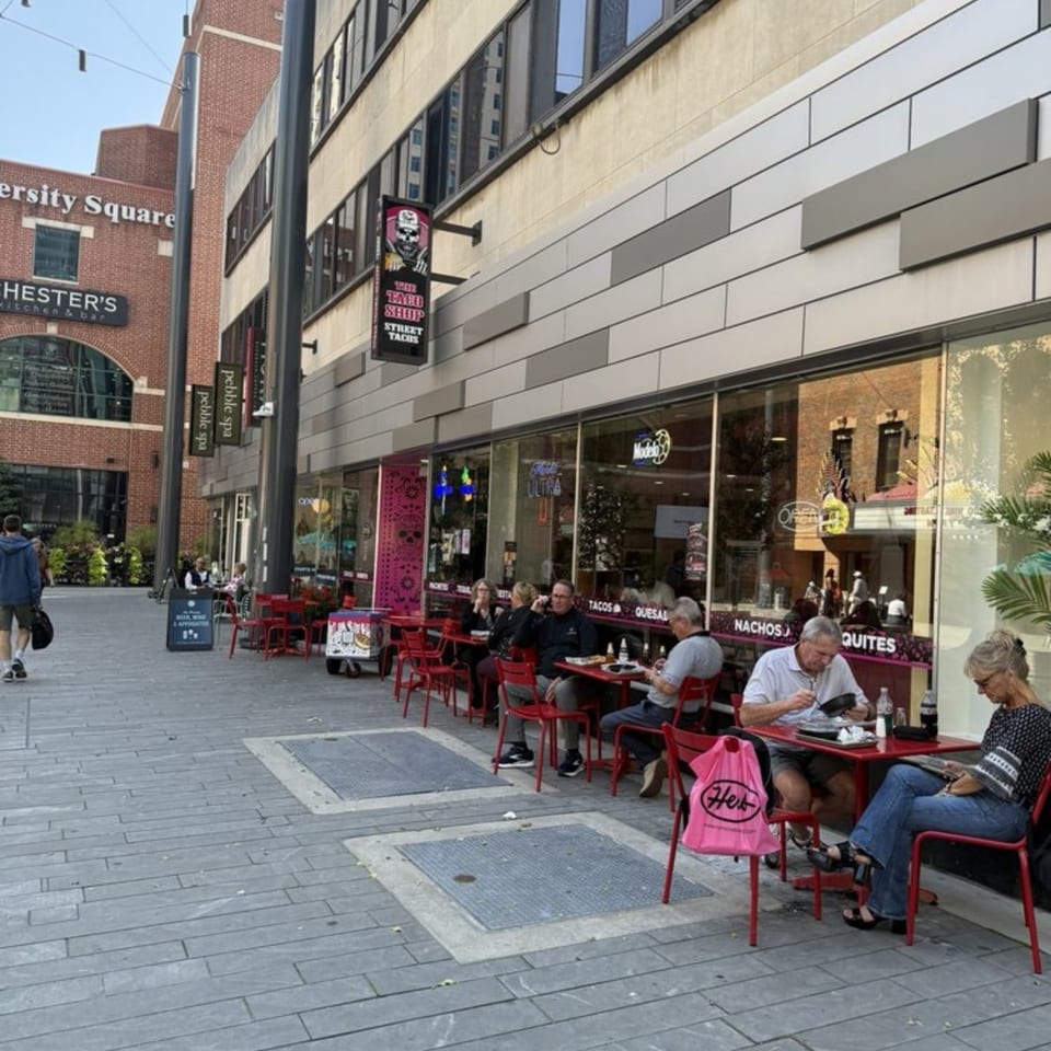 The Taco Shop's outdoor patio with red tables and chairs, and people dining on a city sidewalk.