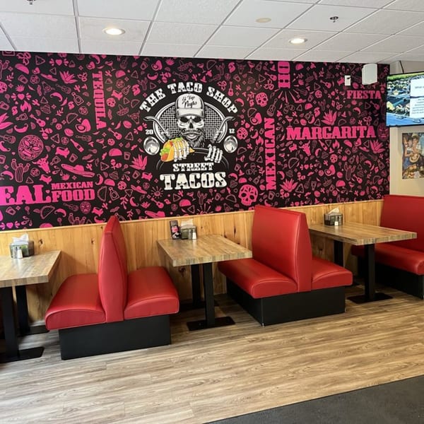 Interior of The Taco Shop with red booths, wooden tables, and a black and pink mural.