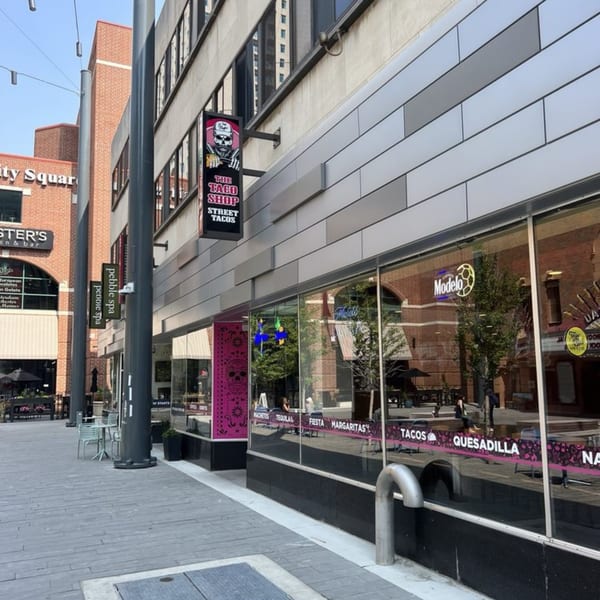 Exterior view of The Taco Shop with its skull logo sign and large windows reflecting the street.