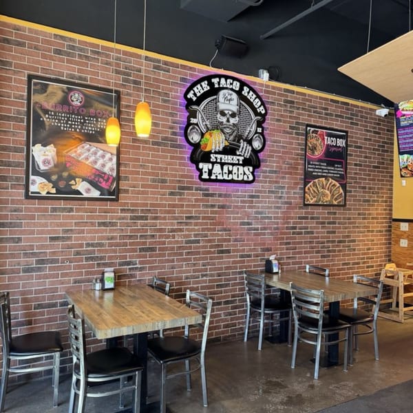 Interior of The Taco Shop with brick walls, wooden tables, metal chairs, and menu posters.
